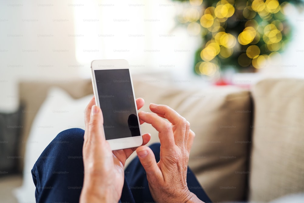 Un gros plan des mains d’une femme âgée avec un smartphone à la maison au moment de Noël. Espace de copie.