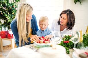 선물과 어머니와 할머니가 크리스마스 시간에 집 테이블에 앉아 있는 작은 소년.