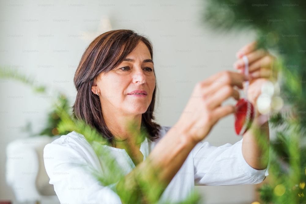 Una donna anziana che tiene un ornamento, decorando un albero di Natale a casa.