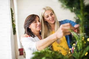 Eine glückliche ältere Frau mit erwachsener Tochter, die zu Hause am Weihnachtsbaum steht.