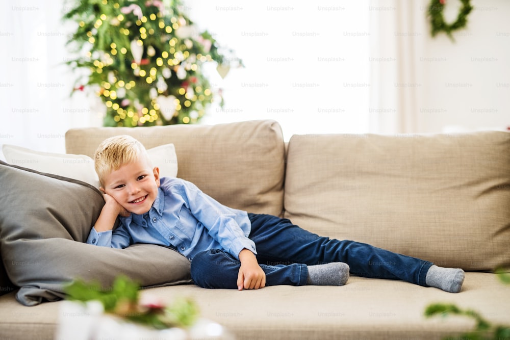 A happy small boy lying on a sofa at home at Christmas time.