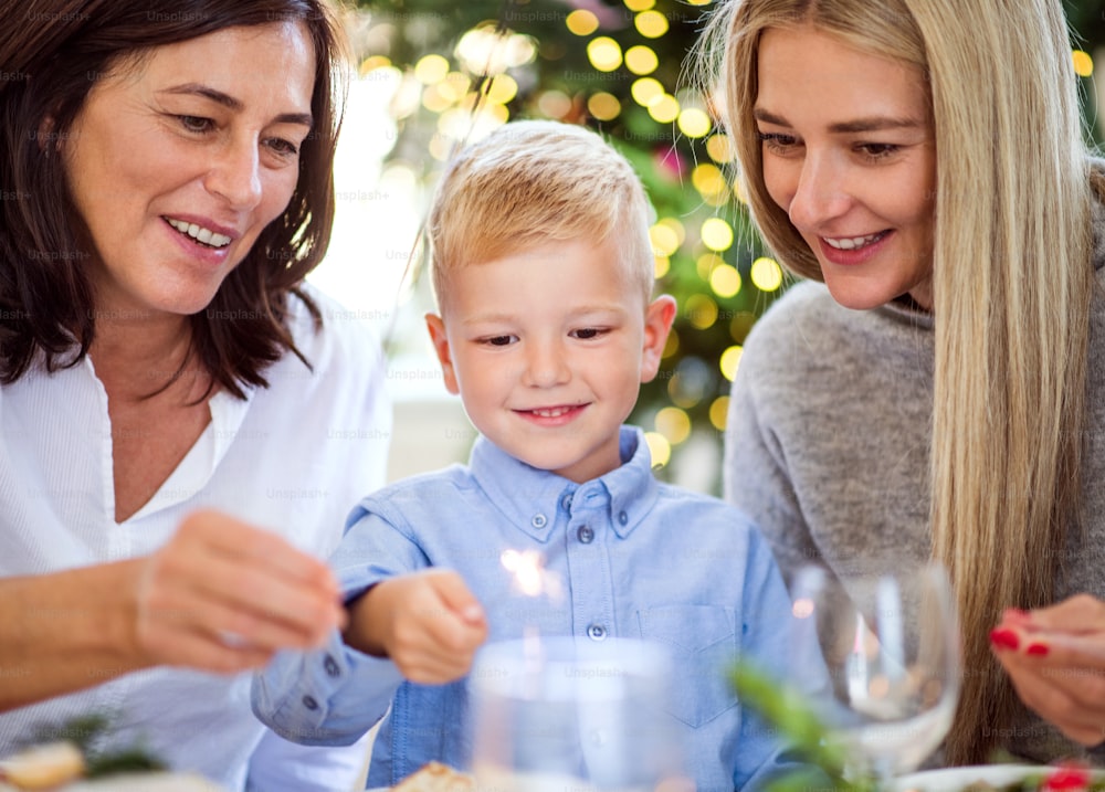 A small boy with mother and grandmother sitting at a table at Christmas time, holding sparkles.