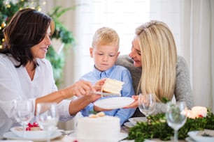 Un niño pequeño con madre y abuela sentadas a la mesa, comiendo un pastel en Navidad.