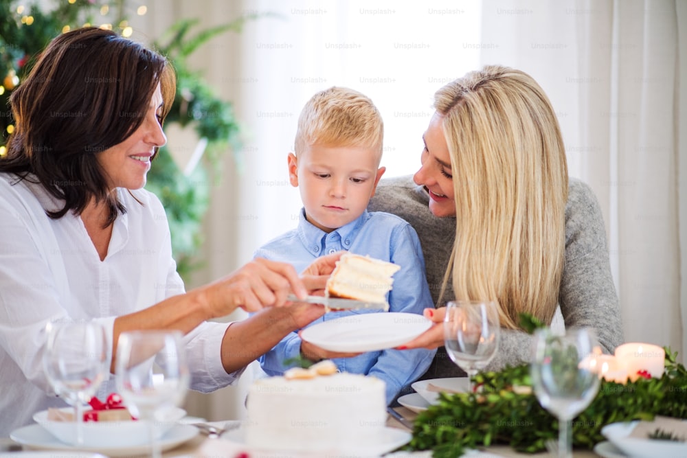 Um menino pequeno com mãe e avó sentados à mesa, comendo um bolo na época do Natal.