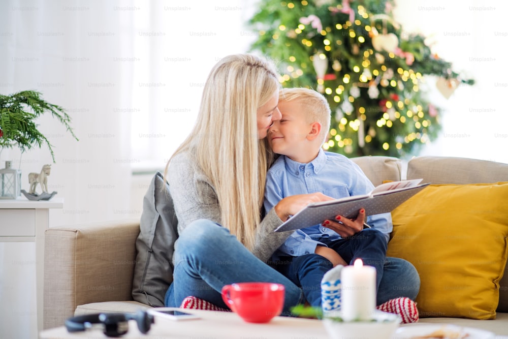 Una madre e un bambino seduti su un divano di casa nel periodo natalizio, leggendo una storia da un libro.