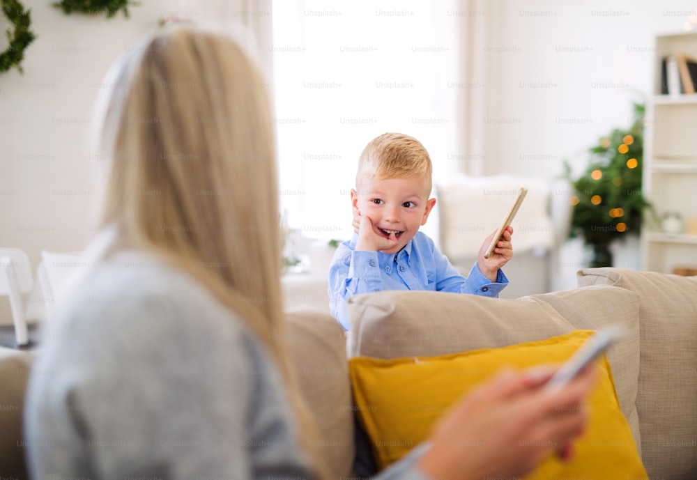 Una madre e un bambino con gli smartphone seduti su un divano di casa nel periodo natalizio, giocando.