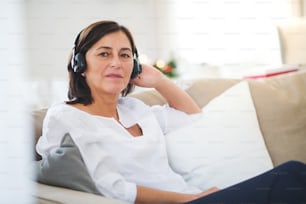 A senior woman with headphones sitting on a sofa at home, listening to music at Christmas time.