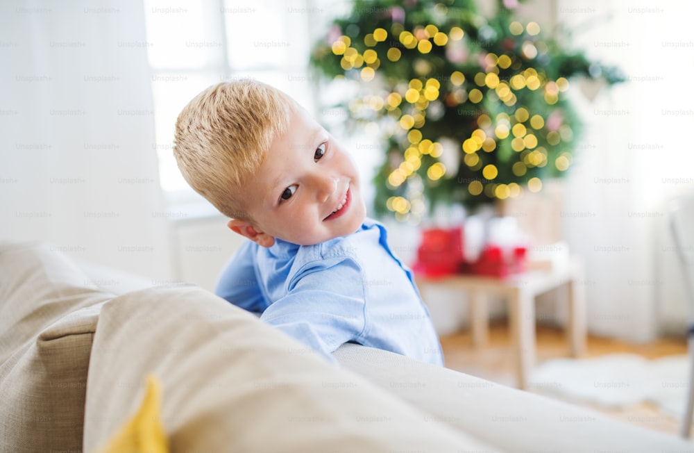 Un primer plano de un niño pequeño apoyado en un sofá en casa en Navidad.