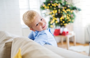 Um close-up de menino pequeno encostado em um sofá em casa na época do Natal.
