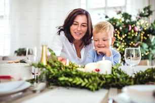 A happy small boy with grandmother sitting at the table at home at Christmas time.