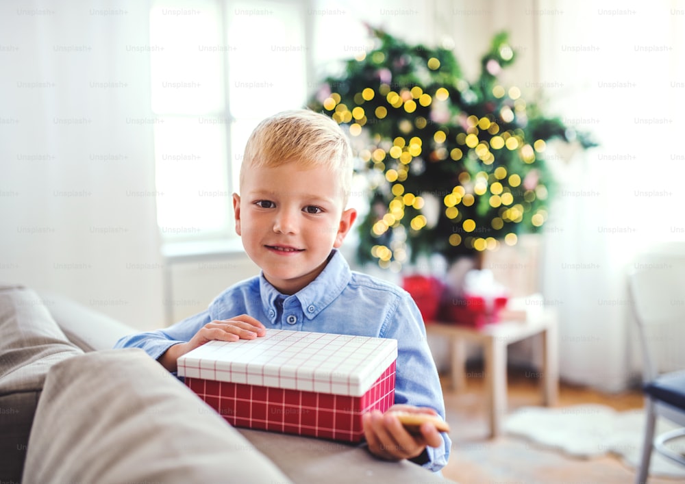 Ein kleiner Junge mit einem Geschenk, der zur Weihnachtszeit zu Hause steht.