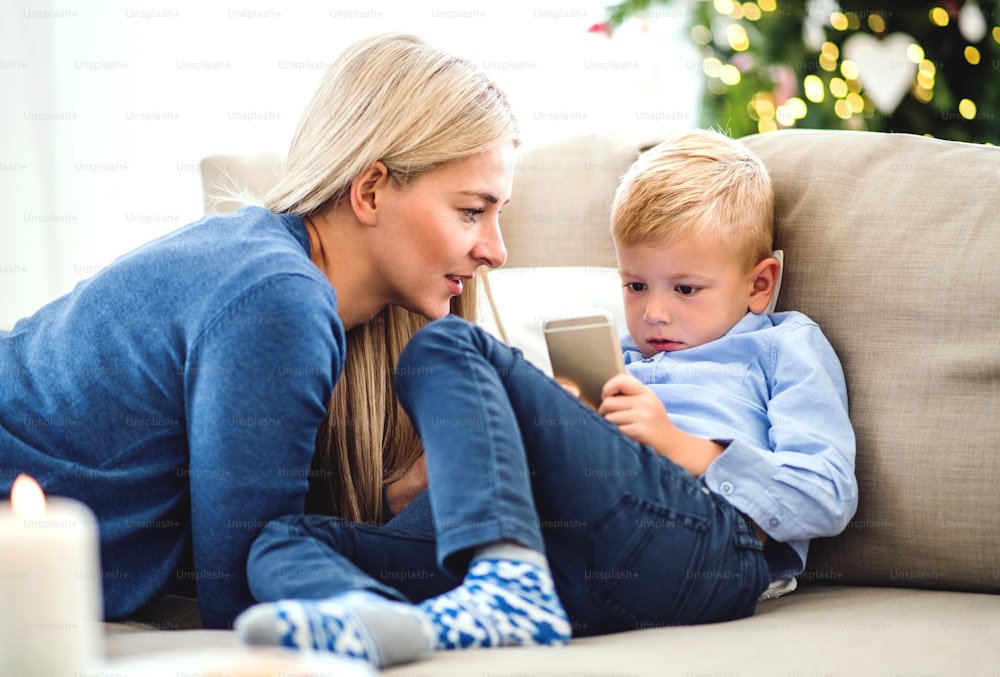 Una madre e un bambino con lo smartphone seduti su un divano di casa nel periodo natalizio, giocando.