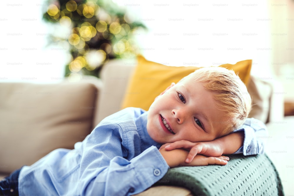Um close-up de menino pequeno deitado em um sofá em casa na época do Natal.
