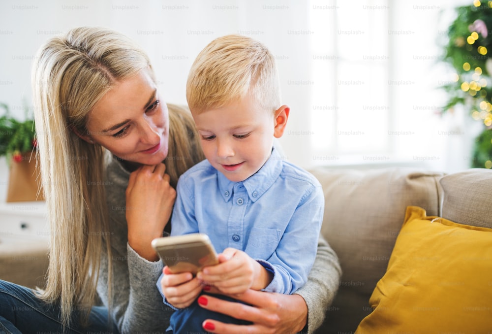 Una madre e un bambino con lo smartphone seduti su un divano di casa nel periodo natalizio, giocando.