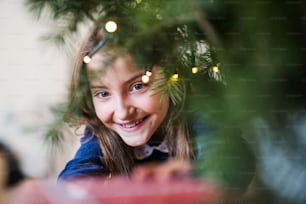A close-up of a small girl standing by a Christmas tree at home. Copy space.