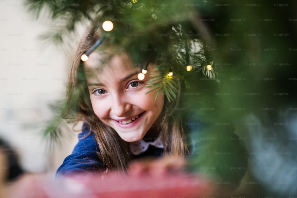 Un primo piano di una bambina in piedi vicino a un albero di Natale a casa. Copia spazio.