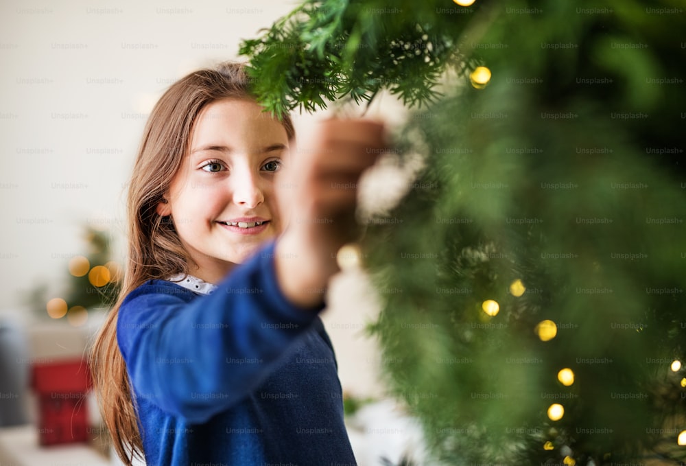 Una bambina in piedi vicino a un albero di Natale a casa. Copia spazio.