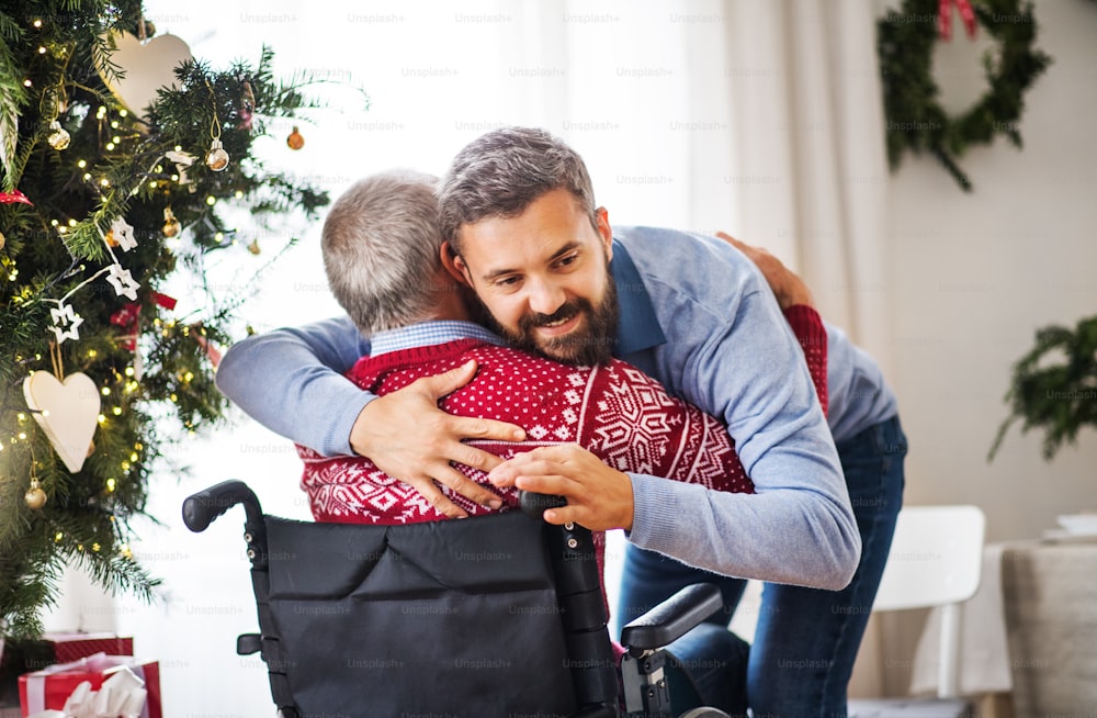 Um homem hipster abraçando seu pai idoso deficiente em cadeira de rodas na época do Natal.