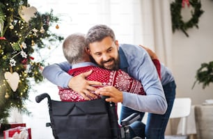 A hipster man hugging his disabled senior father in wheelchair at Christmas time.