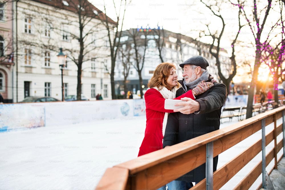 Heureux couple de personnes âgées avec smartphone lors d’une promenade dans une ville en hiver. Un homme et une femme prenant un selfie.