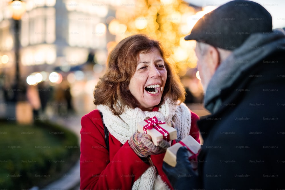 Happy senior couple on an outdoor Christmas market, holding wrapped presents. Winter time.