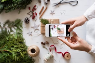 Composição do Natal em um fundo branco. Flat lay. Mãos femininas segurando um smartphone, tirando uma fotografia.