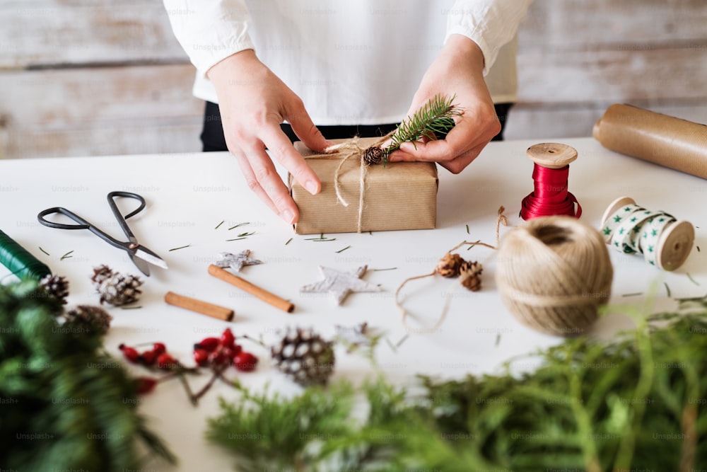 Composición navideña sobre fondo blanco. Manos femeninas decorando un regalo envuelto.