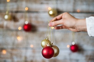 Mão feminina segurando decorações de Natal. Bolas vermelhas e douradas.