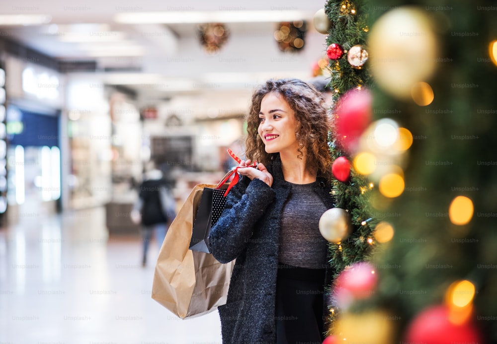 Un retrato de una adolescente feliz con bolsas de papel en un centro comercial en Navidad. Espacio de copia.