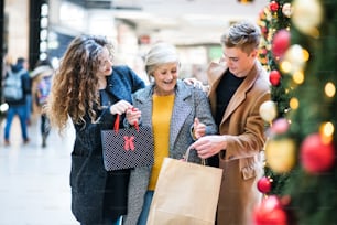 A portrait of senior grandmother and teenage grandchildren with paper bags standing in shopping center at Christmas time.