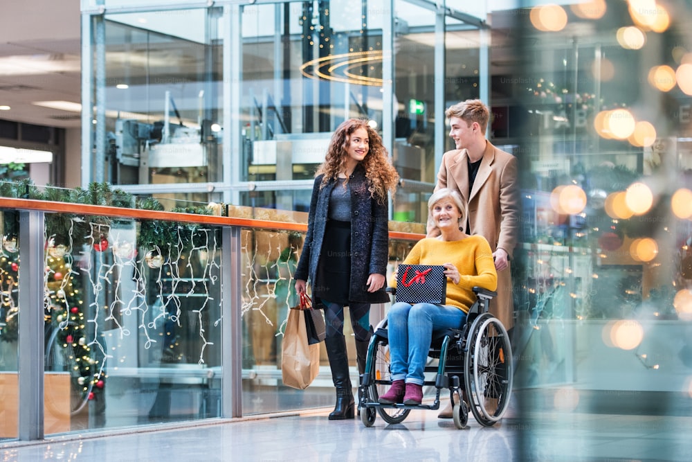 휠체어를 탄 할머니와 10대 손주들이 크리스마스 때 쇼핑센터를 걷고 있다.