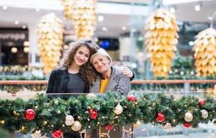 A portrait of senior grandmother and teenage granddaughter standing in shopping center at Christmas time.