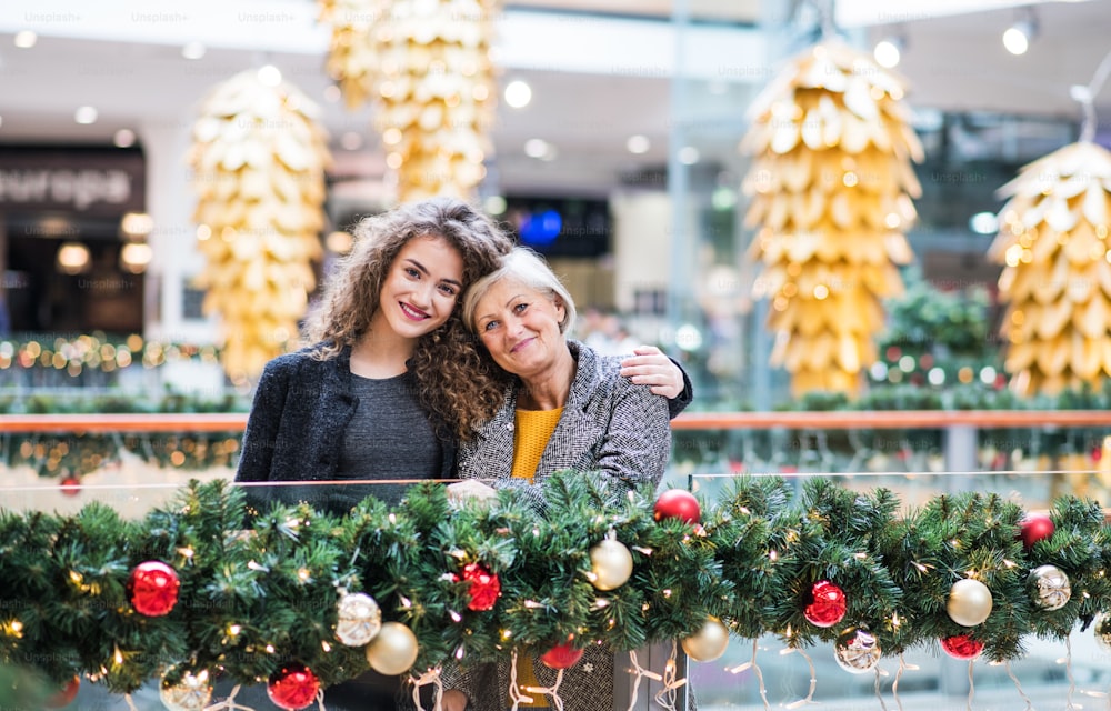 Un retrato de la abuela mayor y la nieta adolescente de pie en el centro comercial en Navidad.