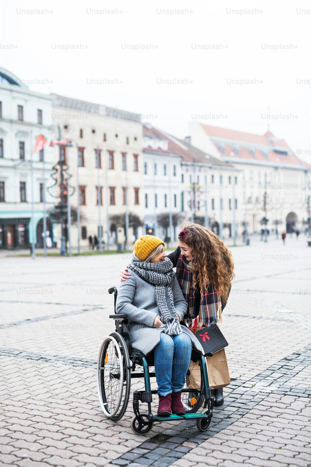 A teenager girl with disabled grandmother in wheelchair outdoors on the street in winter, talking.
