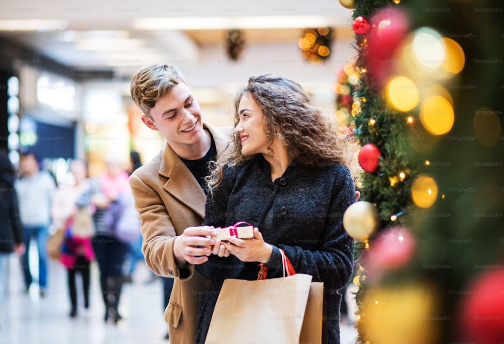 Um jovem feliz dando um presente para sua amiga no shopping center na época do Natal. Espaço de cópia.