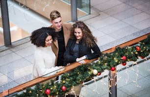 A high-angle view of young friends standing in shopping center at Christmas time.