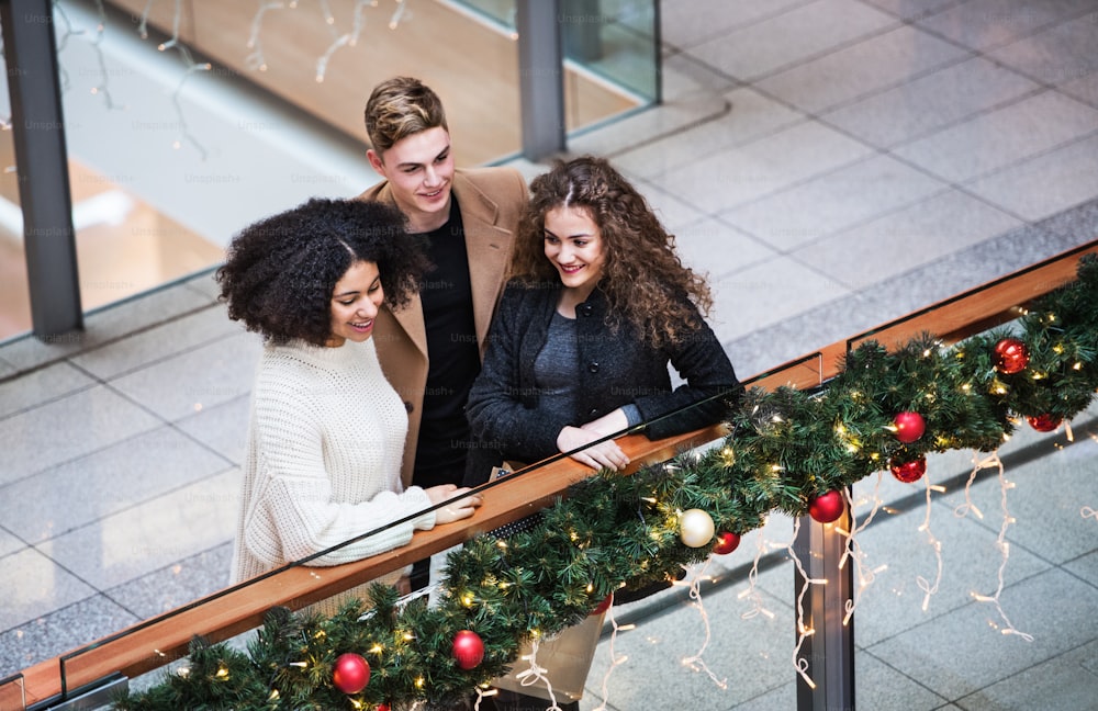 A high-angle view of young friends standing in shopping center at Christmas time.