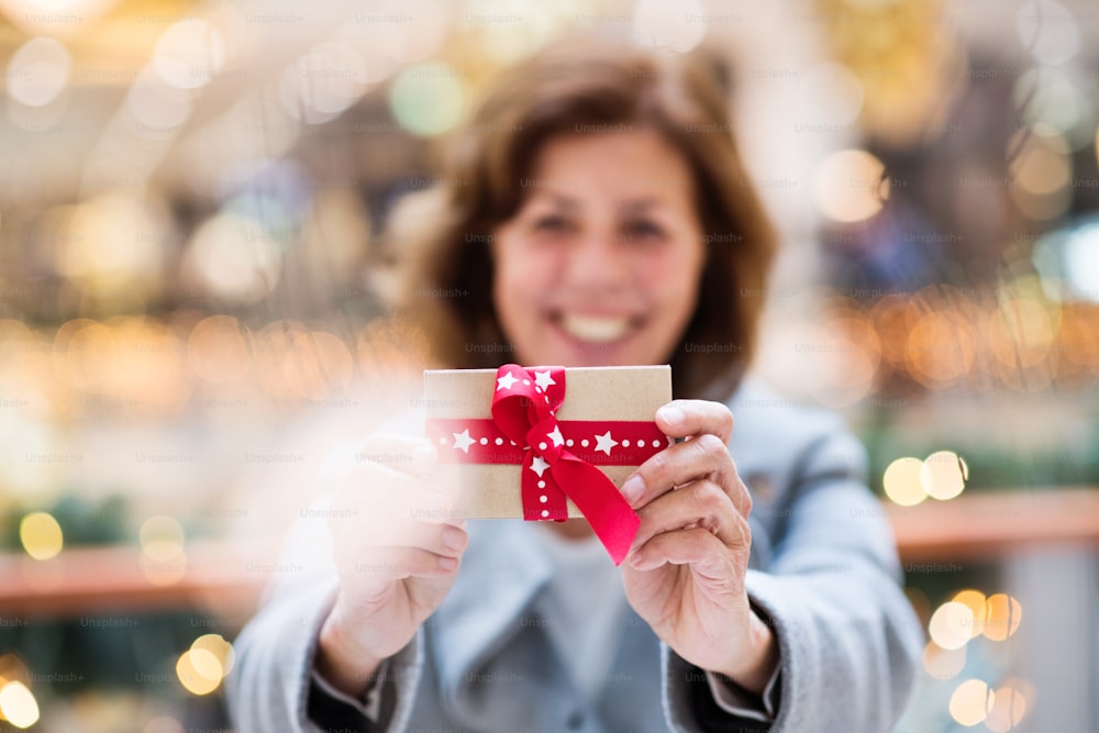 A senior woman holding a present in shopping center at Christmas time.