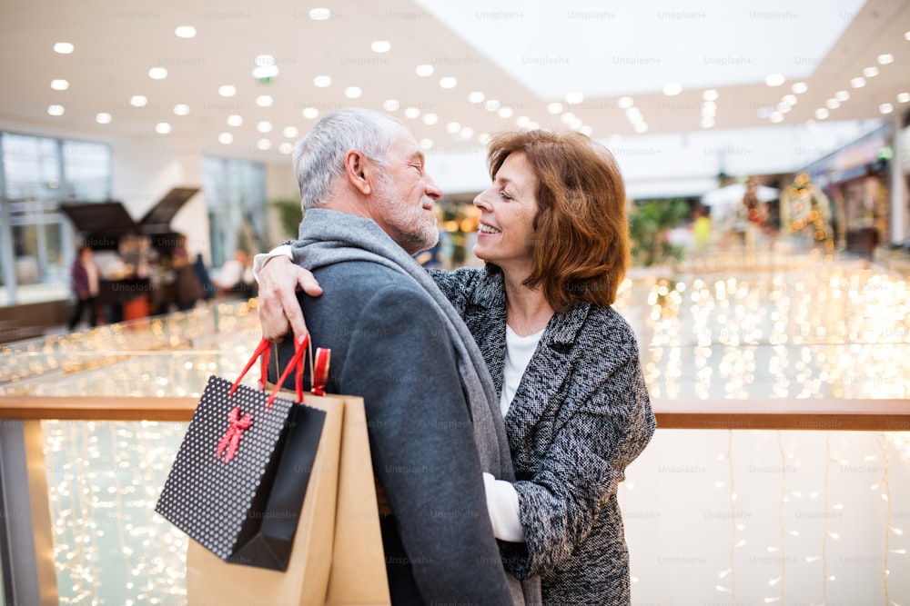 Feliz pareja de ancianos con bolsas de papel en el centro comercial mirándose, abrazándose.