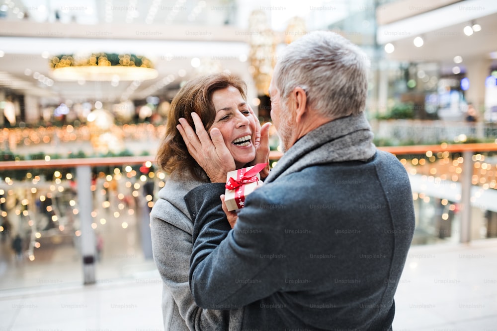 Un homme âgé offrant un cadeau à une femme heureuse au centre commercial au moment de Noël.