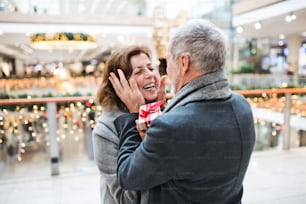 A senior man giving a present to a happy woman at shopping center at Christmas time.