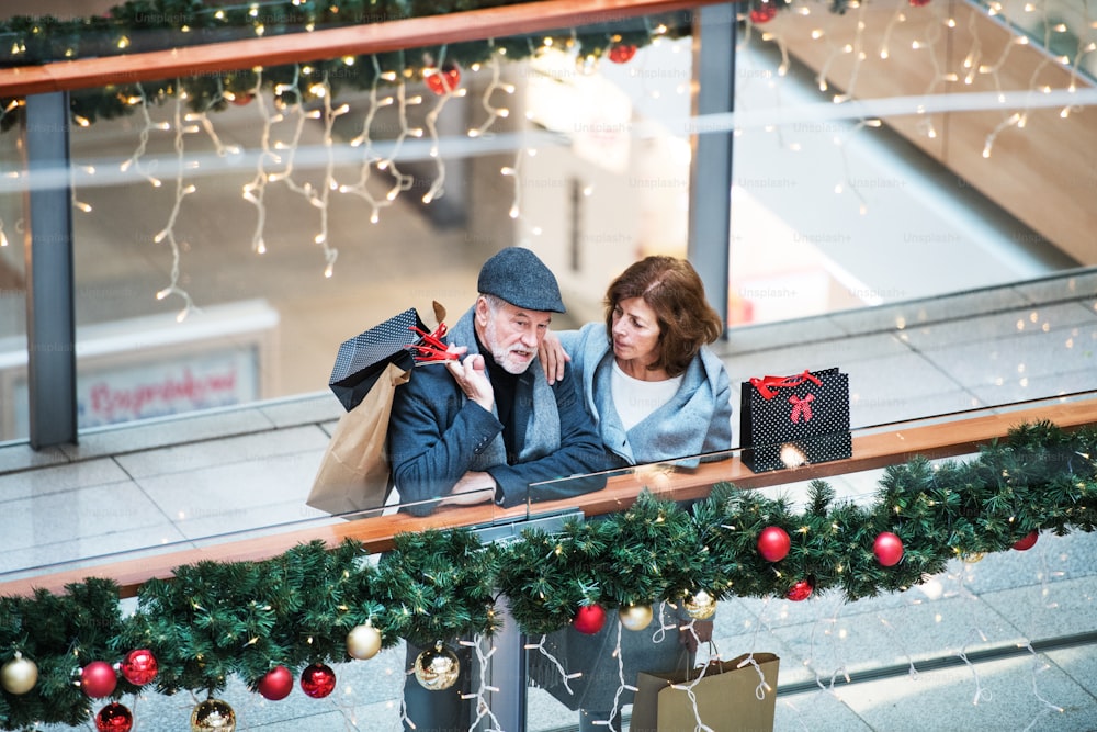 A high angle view of senior couple with paper bags in shopping center at Christmas time.