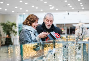 Une femme âgée heureuse offrant un cadeau à un homme dans un centre commercial au moment de Noël.