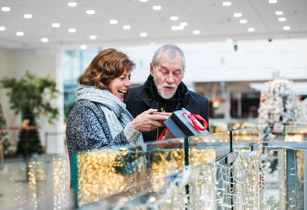 A happy senior woman giving a present to a man in shopping center at Christmas time.