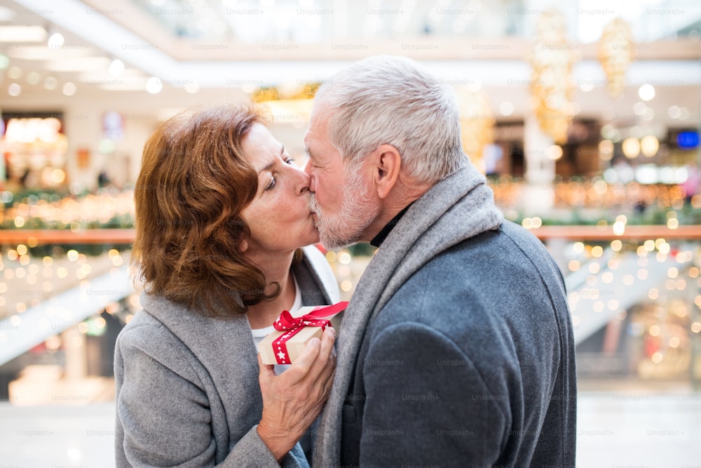 Senior couple doing Christmas shopping. A man giving a present to a woman. Shopping center at Christmas time.
