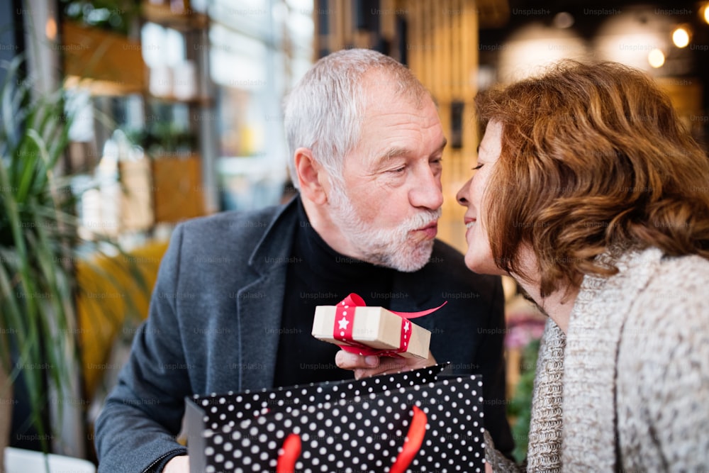 Pareja mayor haciendo compras navideñas. Un hombre dando un regalo a una mujer. Centro comercial en época navideña.