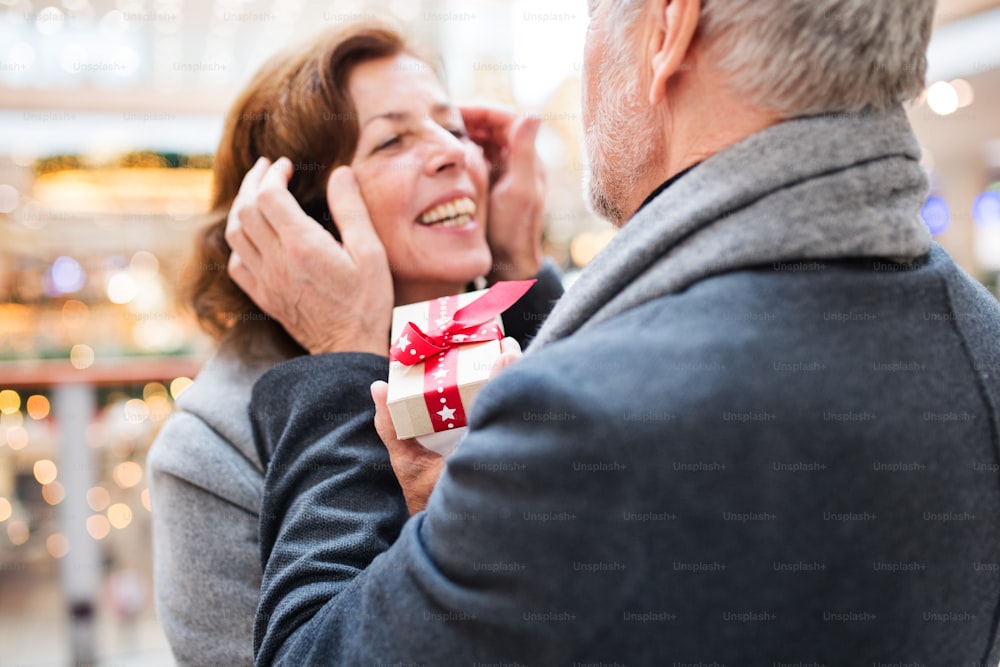 Casal de idosos fazendo compras de Natal. Um homem irreconhecível dando um presente a uma mulher. Shopping center na época do Natal.