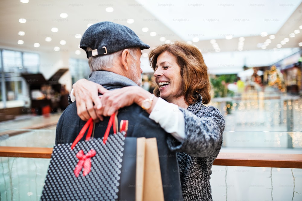 Feliz pareja de ancianos con bolsas de papel en el centro comercial mirándose, abrazándose.