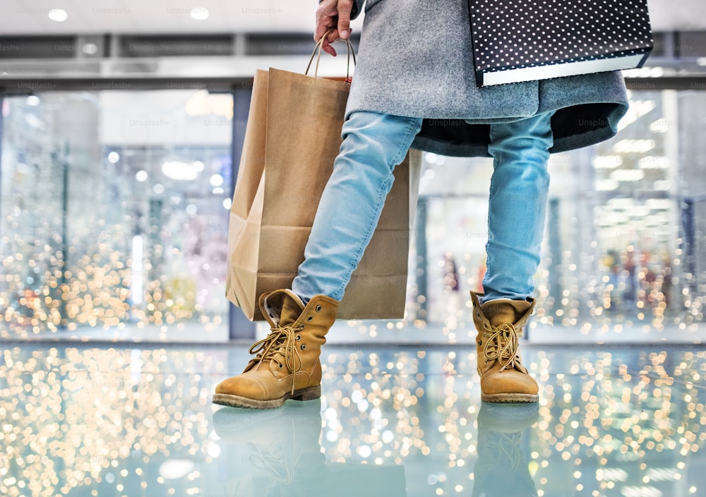 Pernas de mulher idosa irreconhecível com saco de papel fazendo compras de Natal. Shopping center na época do Natal.