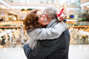 Senior couple doing Christmas shopping. A man giving a present to a woman. Shopping center at Christmas time.